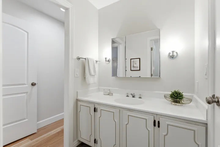 White vanity with decorative cabinet fronts, single basin sink, wall-mounted faucet, and a large mirrored medicine cabinet
