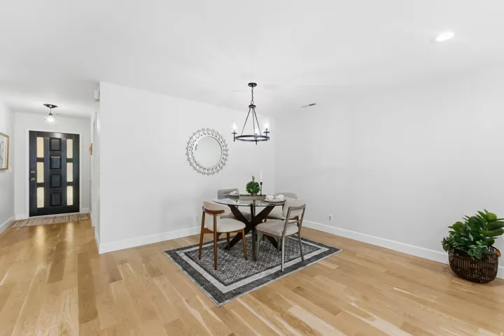 Wood-finish flooring throughout, featuring a modern black front door with frosted glass panels, and a drum-style chandelier