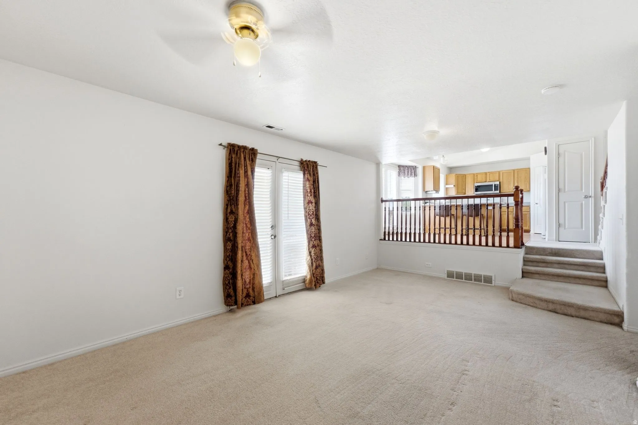 Spacious open-concept living area featuring neutral carpeting, recessed ceiling lighting, and glass sliding doors with brown curtain panels