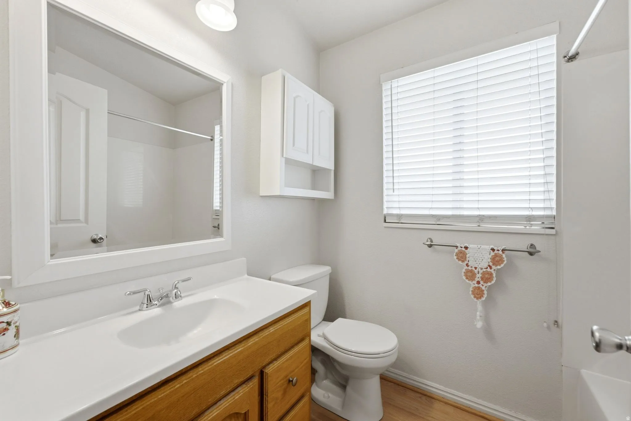 Bathroom featuring a wood-finish vanity with a white countertop, chrome faucet, wall-mounted mirror, and a window with blinds