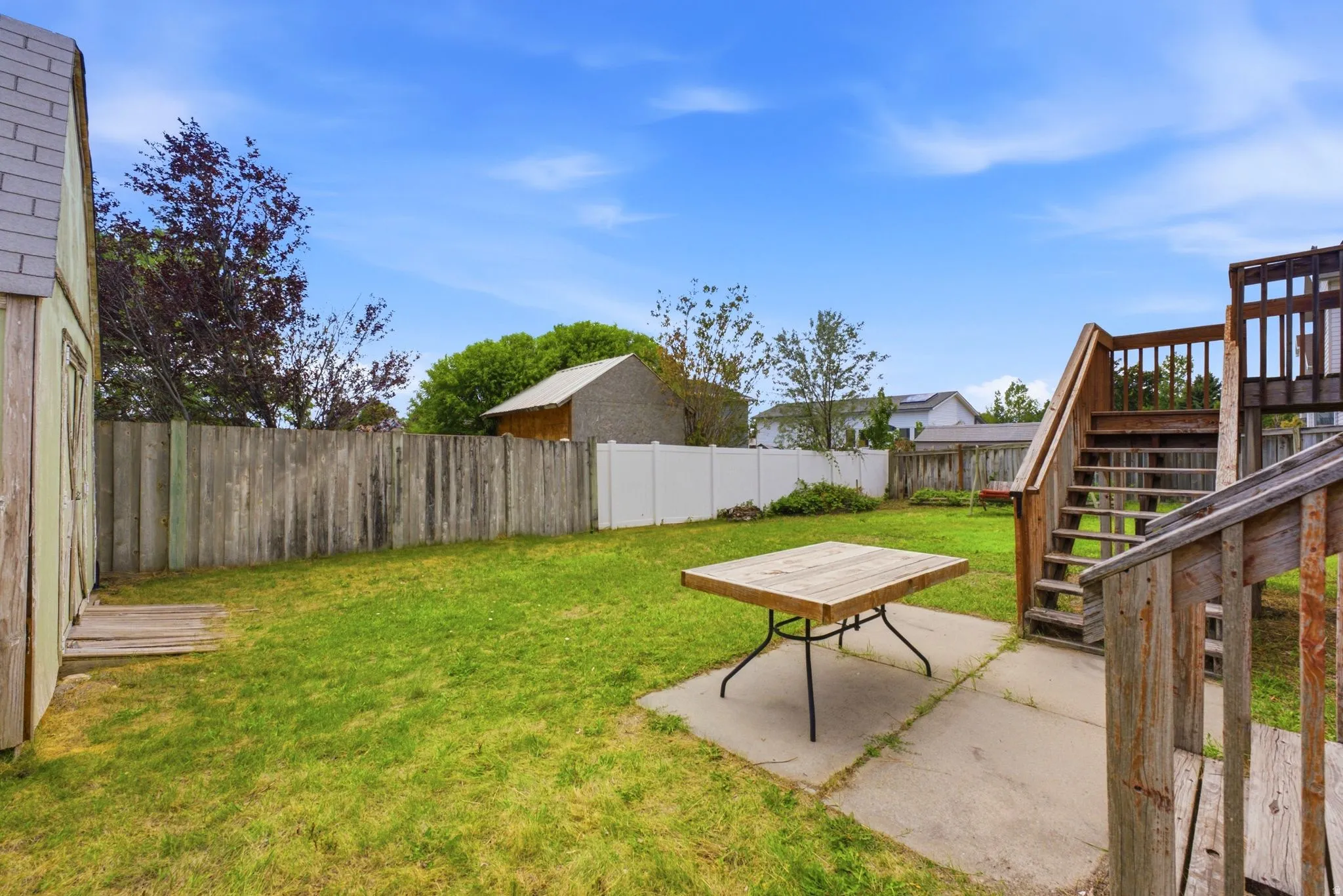 Expansive backyard featuring a lush lawn, wooden privacy fencing, a separate white vinyl fence, a wooden shed, and a wooden deck with stairs