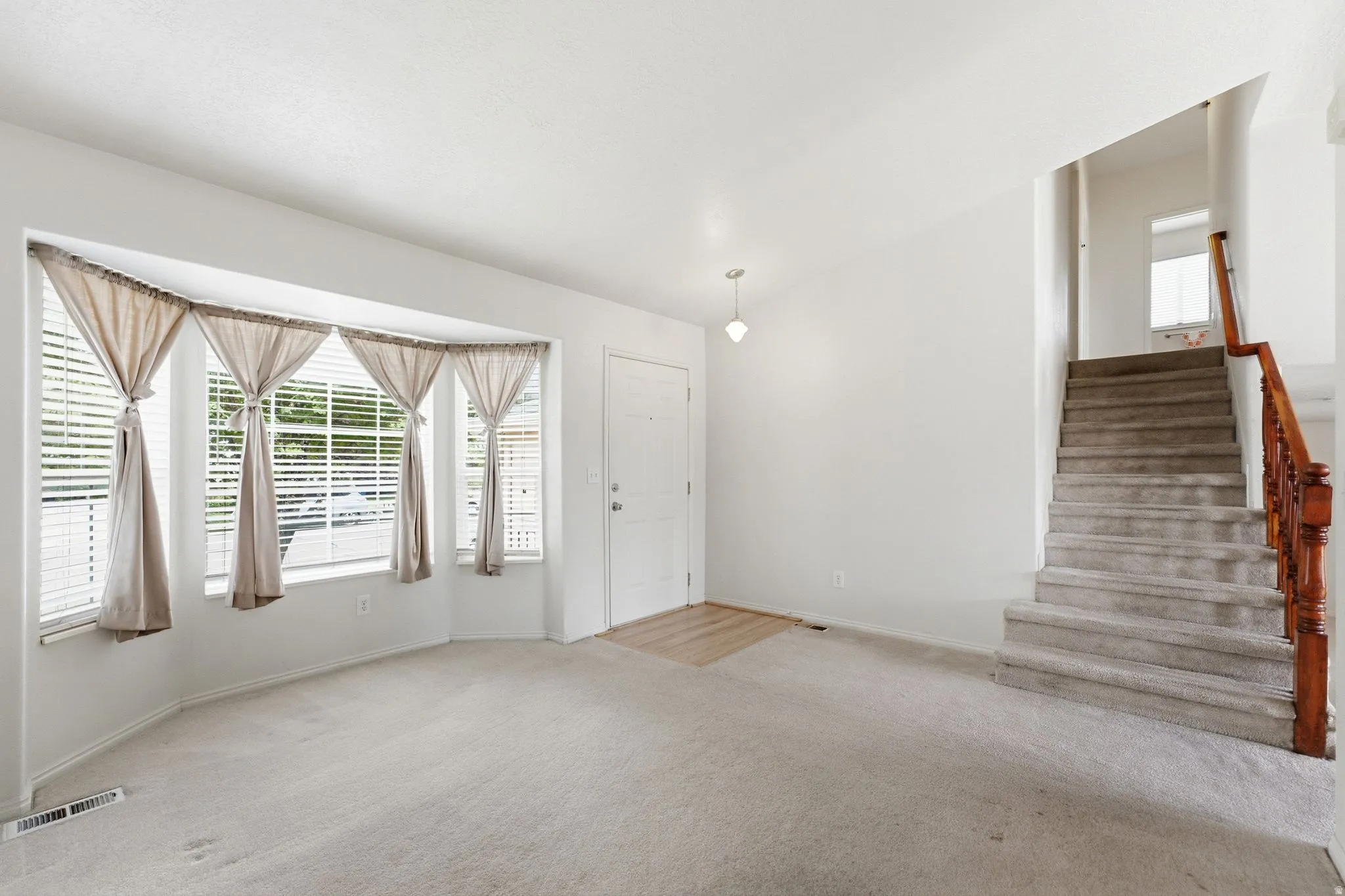 Bay window with blinds, carpeted flooring, wood-finish flooring, staircase with wood railing, recessed lighting