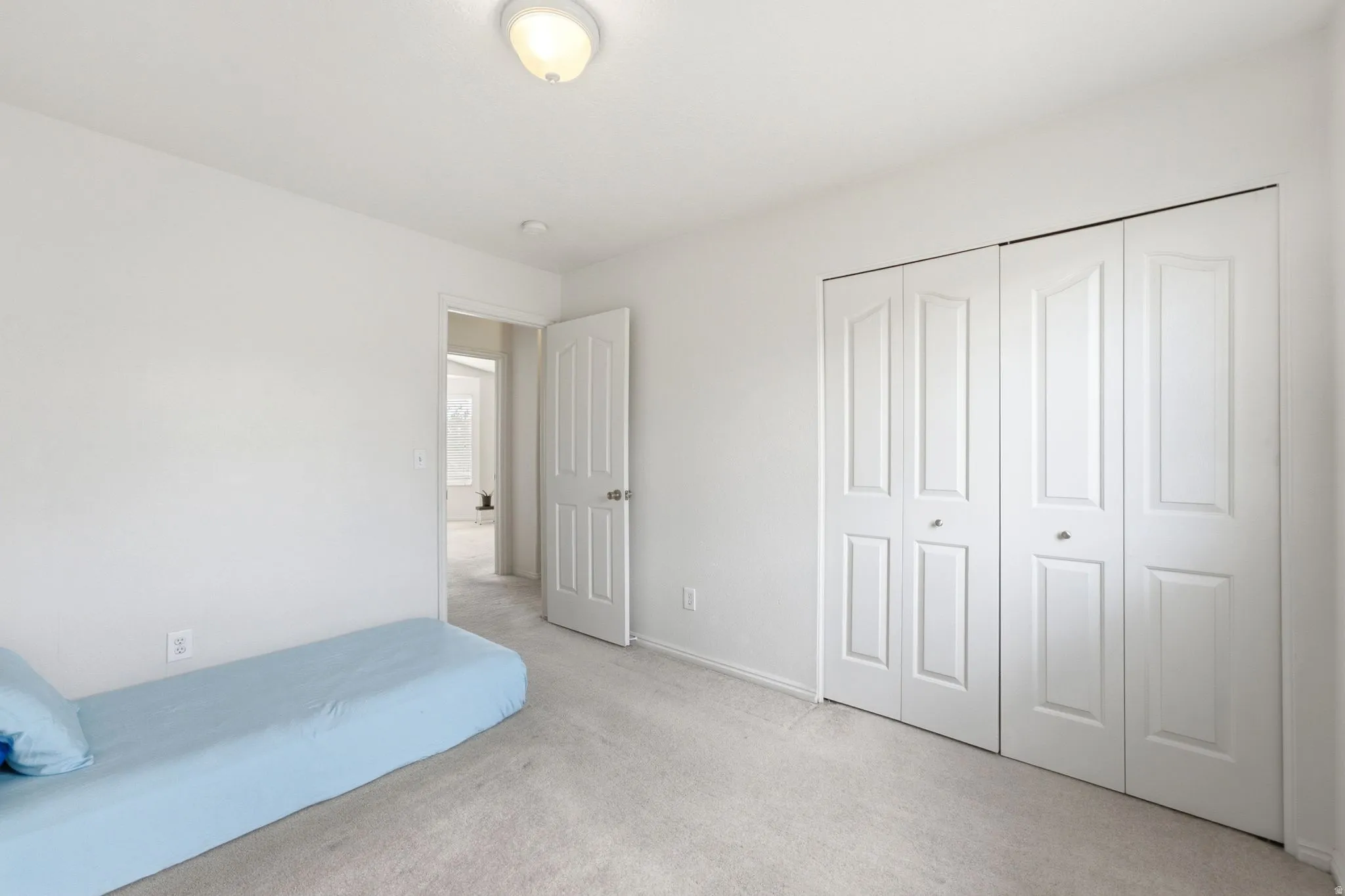 White bi-fold closet doors with panel detailing, light neutral carpeting, and a ceiling-mounted light fixture