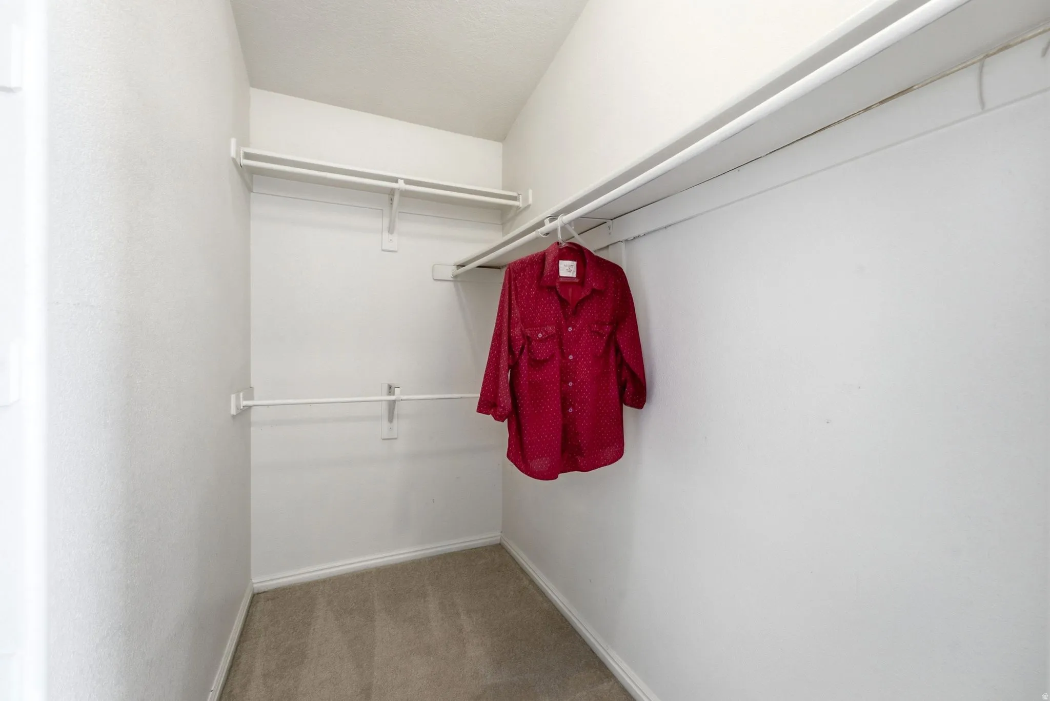Carpeted walk-in closet with multiple white wire shelving units and hanging rods