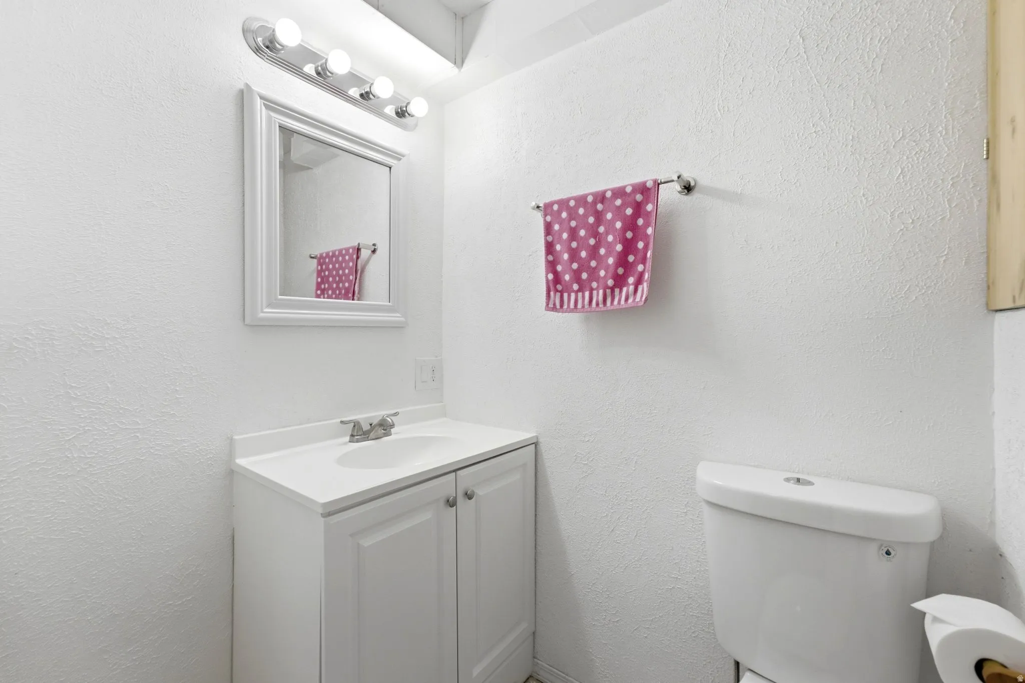 White vanity with a built-in sink, framed mirror, and a four-bulb light fixture