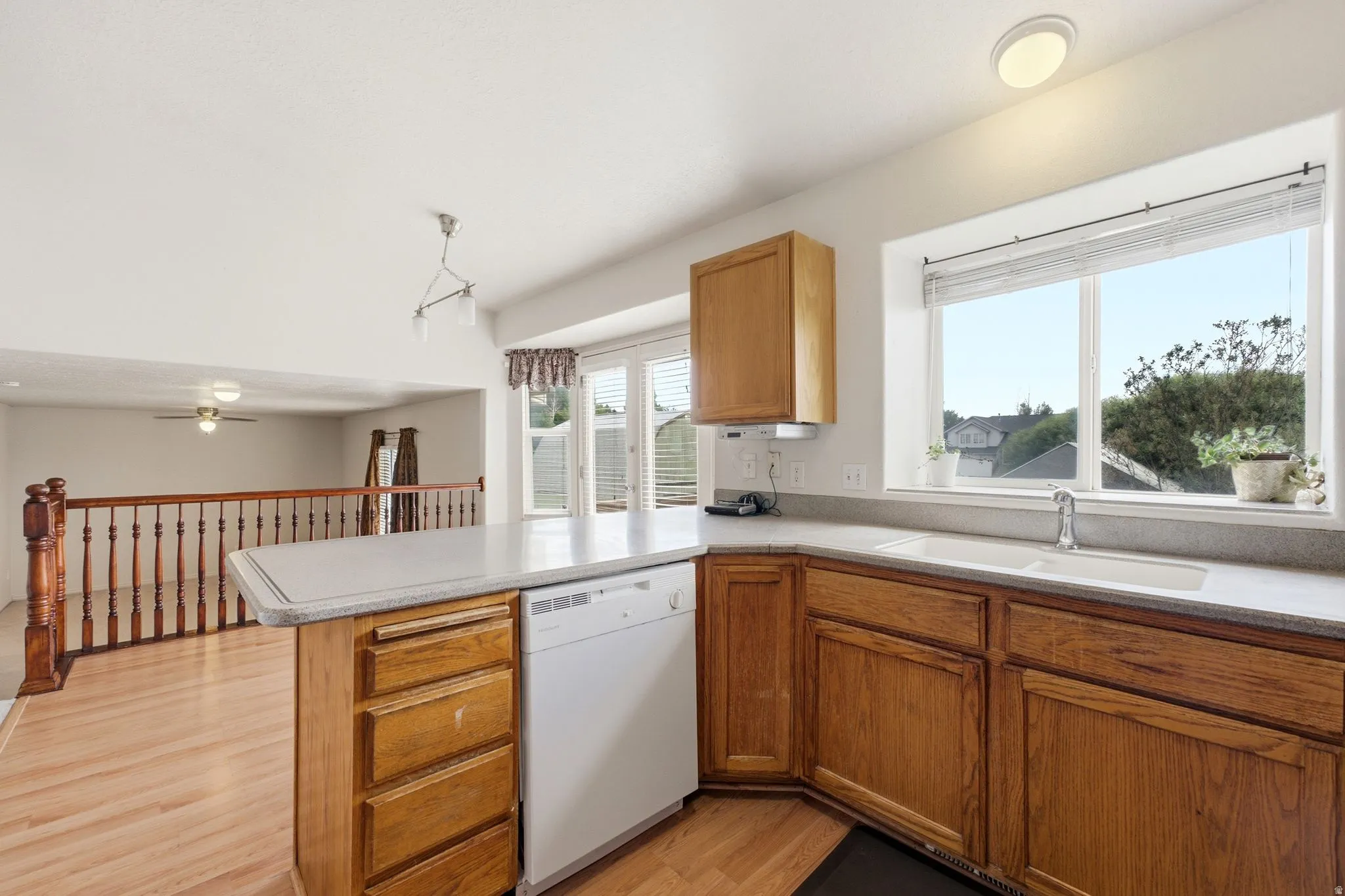 Kitchen featuring wood cabinetry, light-toned countertops, a built-in dishwasher, and a double-basin sink