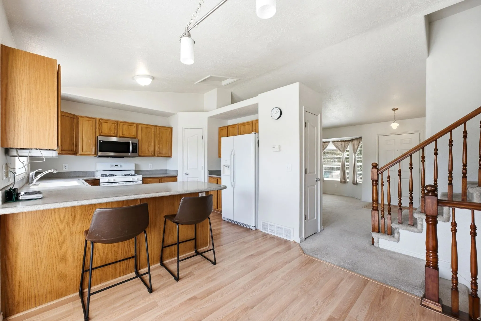 Kitchen featuring wood-finish flooring, light wood cabinetry, stainless steel microwave, and white appliances