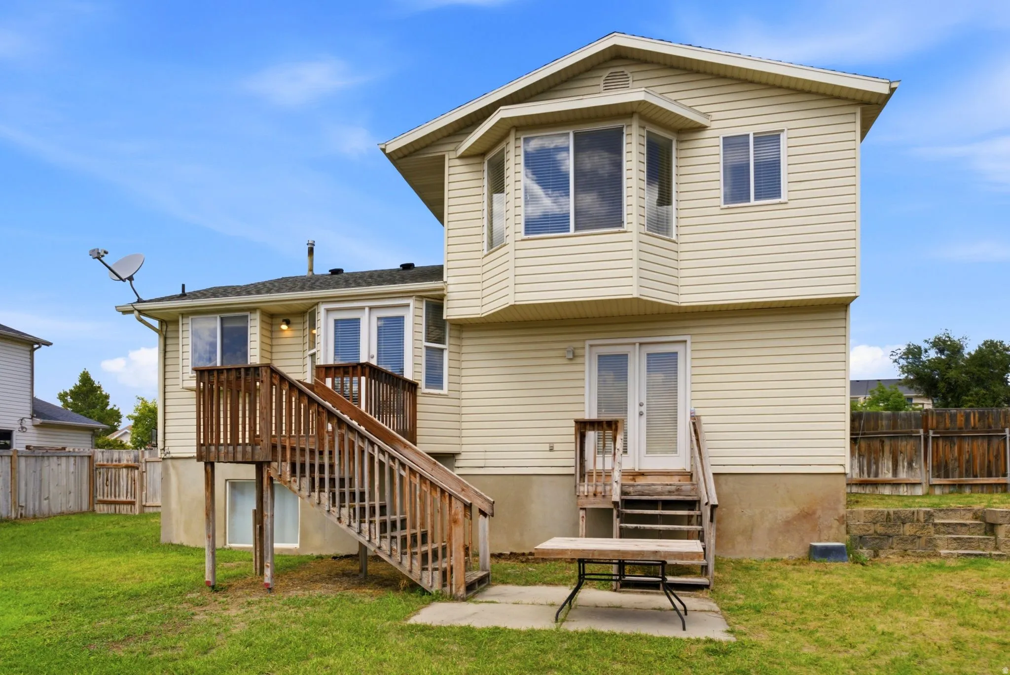 Two-story home featuring cream-colored vinyl siding, multiple windows with dark trim, and a covered front entrance with wooden deck stairs