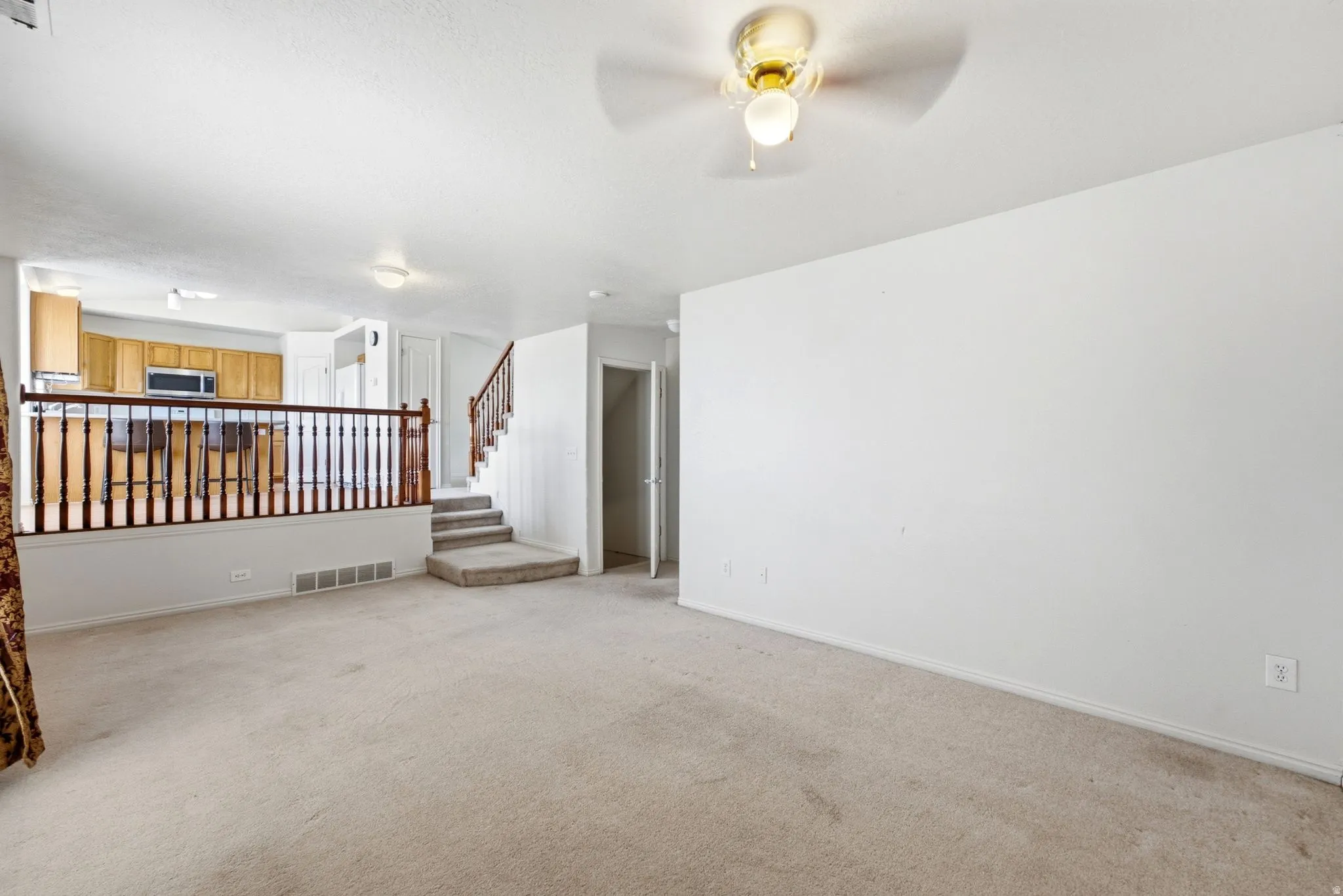 Expansive carpeted area with a ceiling fan light fixture, an open doorway, and a partially visible staircase with wood newel posts