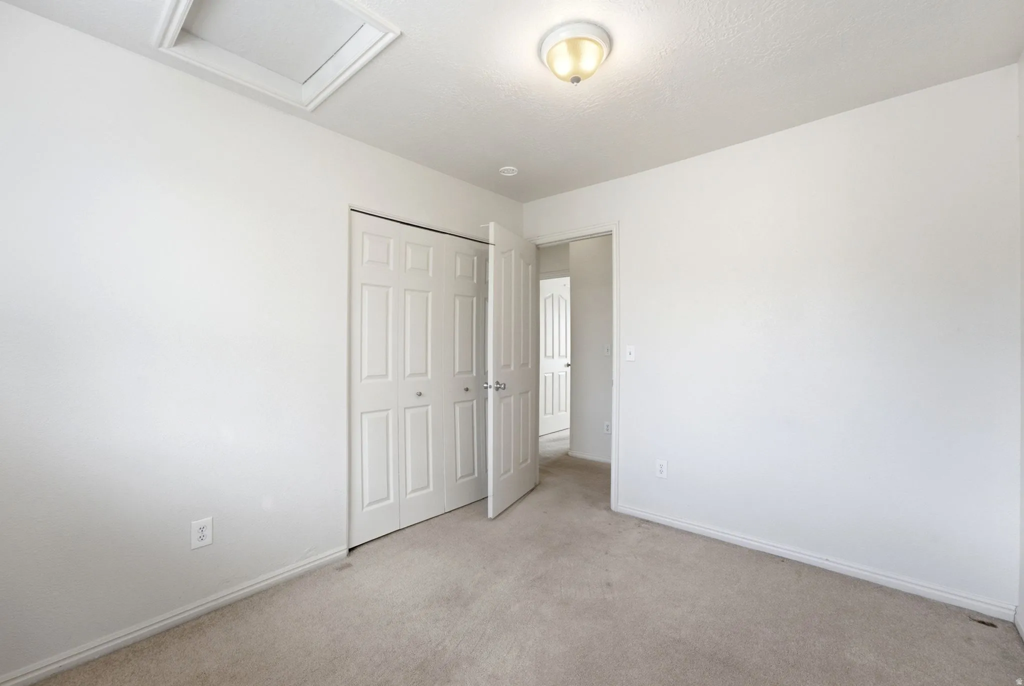 Light-toned carpeted flooring, white painted walls, white bi-fold closet doors, and flush-mount ceiling lighting