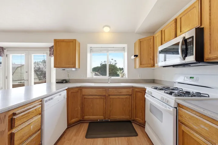 Kitchen featuring wood cabinetry, light-toned countertops, a white gas range, and a built-in microwave