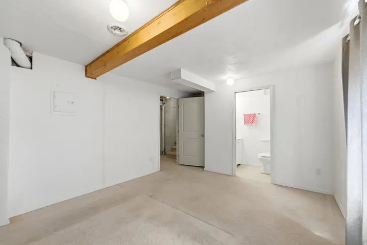 Carpeted interior space featuring a visible wood beam, overhead lighting, and white walls