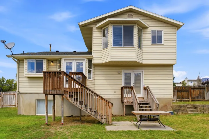 Rear exterior with beige siding, a bay window, and two sets of wood stairs leading to exterior doors