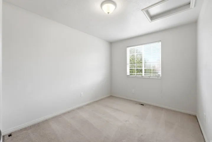 Carpeted flooring, single window with blinds, ceiling-mounted light fixture, white walls, attic access