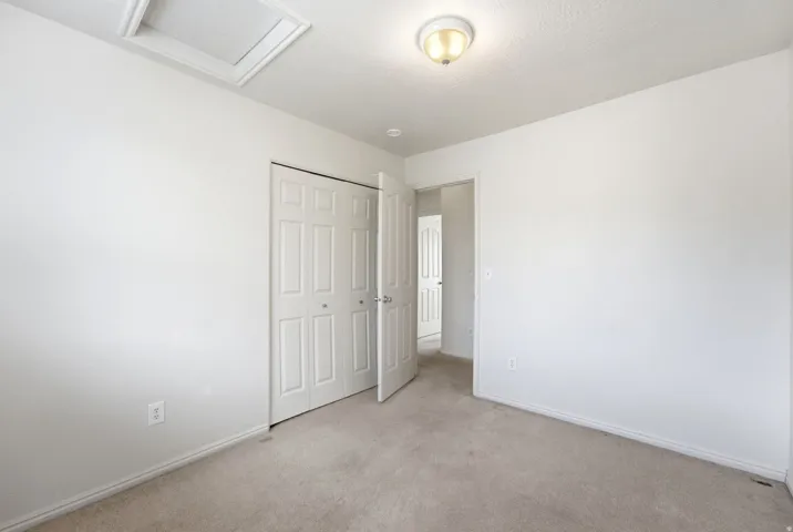 Light-toned carpeted flooring, white painted walls, white bi-fold closet doors, and flush-mount ceiling lighting