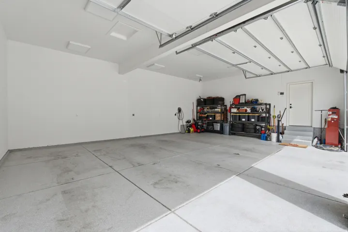 Spacious garage with light-toned concrete flooring, white walls, and overhead lighting