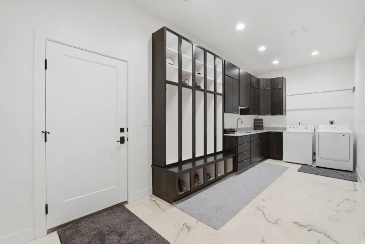 Spacious utility room featuring built-in cabinetry, an integrated sink, white appliances, and light-toned flooring