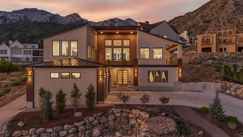 Modern architectural design with multiple large windows, a prominent wood-clad entryway, and exterior wall sconces
