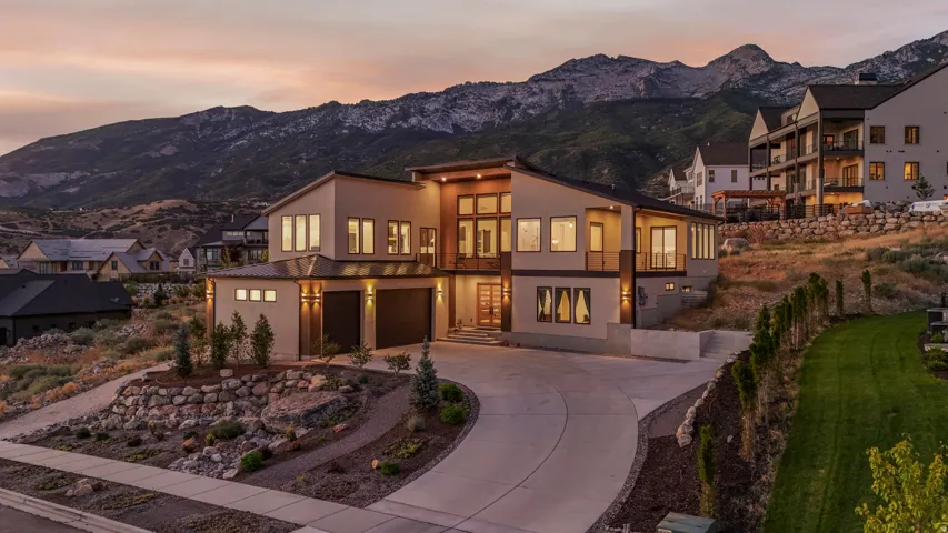 Modern exterior design with large windows, an integrated two-car garage, terraced landscaping, and a paved driveway