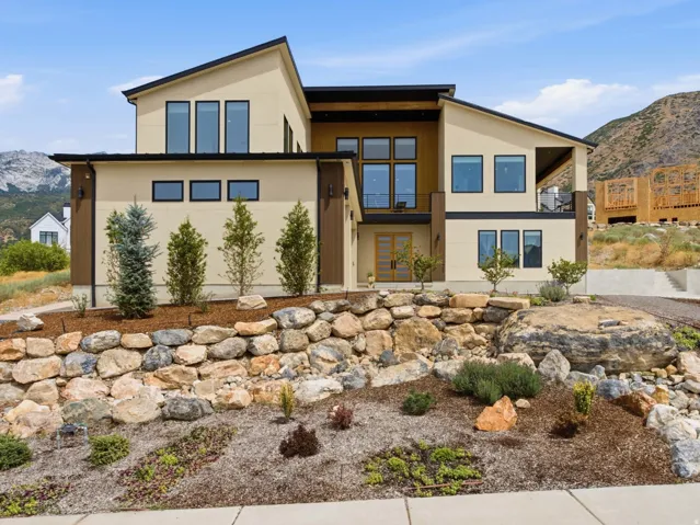 Modern architectural design with multiple large windows, a covered balcony, and a stone retaining wall