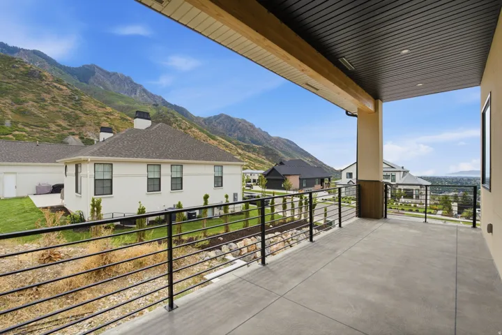 Covered outdoor patio with a concrete surface, black metal railings, and exposed wood beam accents