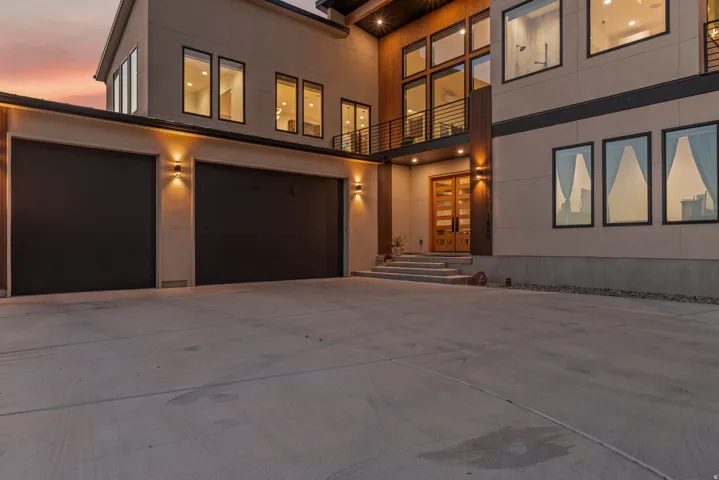 Modern exterior with a large concrete driveway, two dark garage doors, and a wood-paneled entry featuring a double door