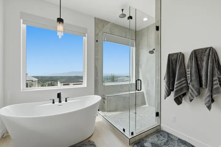 Freestanding soaking tub with matte black fixtures, glass-enclosed shower with integrated bench, and a large window