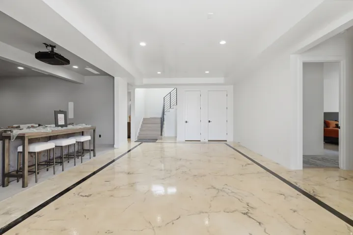 Polished stone flooring with contrasting inlay, recessed lighting, white walls, and a staircase with a metal railing