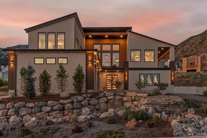 Modern architectural design featuring varied rooflines, extensive window placements, and a natural stone retaining wall