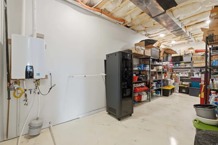 Tankless water heater, exposed ceiling joists with insulation, ductwork, painted concrete flooring, and built-in shelving