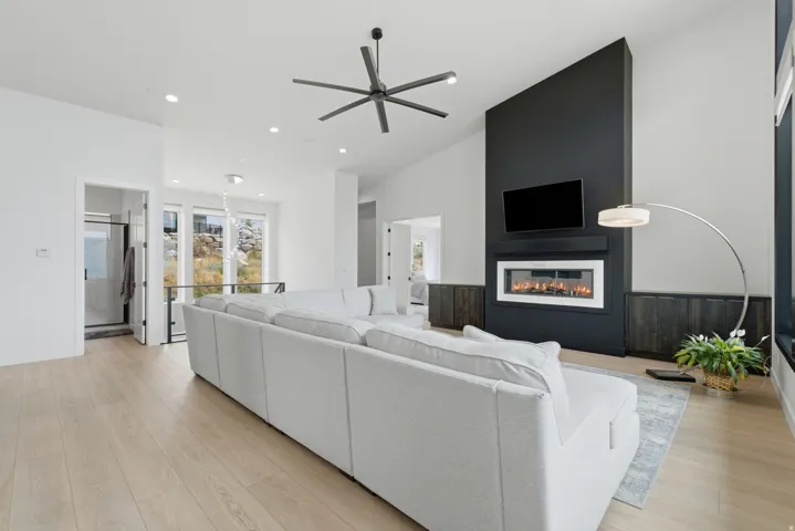 Vaulted ceiling with an attached ceiling fan, light wood-finish flooring, and a contemporary fireplace with a sleek black surround
