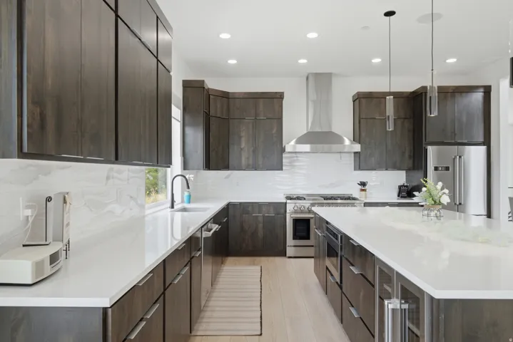 Modern kitchen featuring dark wood-finish cabinetry, light countertops, stainless steel appliances, a range hood, and pendant lighting