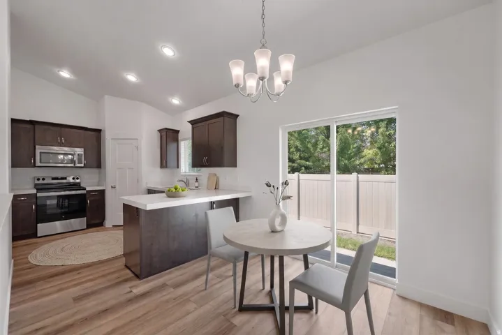 Open-concept kitchen and dining area featuring wood-finish flooring, dark wood cabinetry, stainless steel appliances, and a sliding glass door