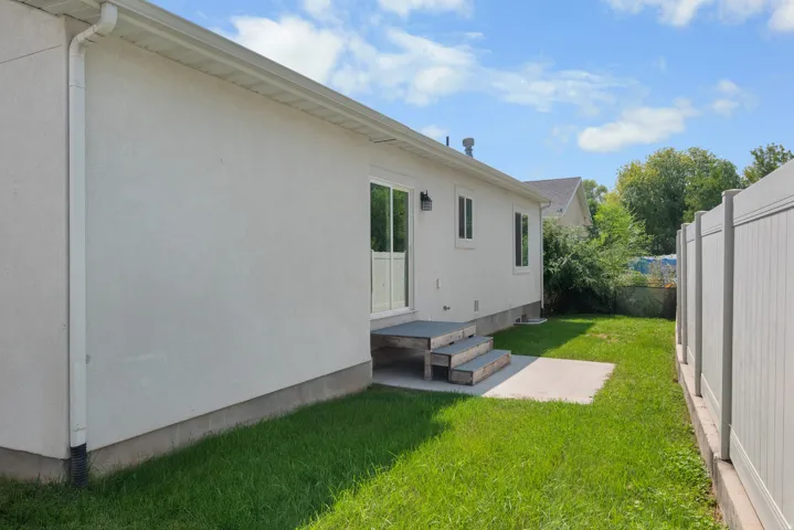 Stucco exterior with a sliding glass door, elevated wood steps, concrete patio, and a privacy fence