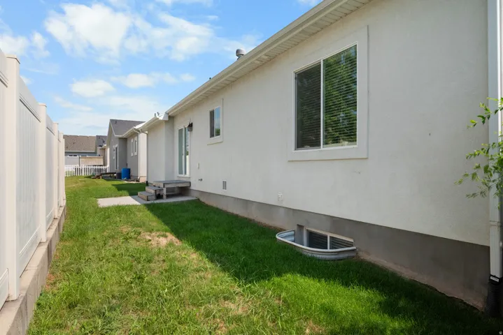 Exterior stucco siding with white trim windows and a white vinyl fence
