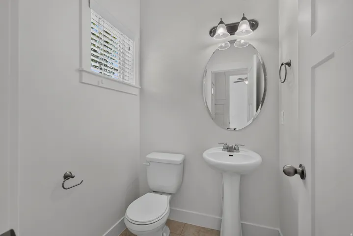 Pedestal sink with chrome faucet, oval mirror, and overhead vanity lighting