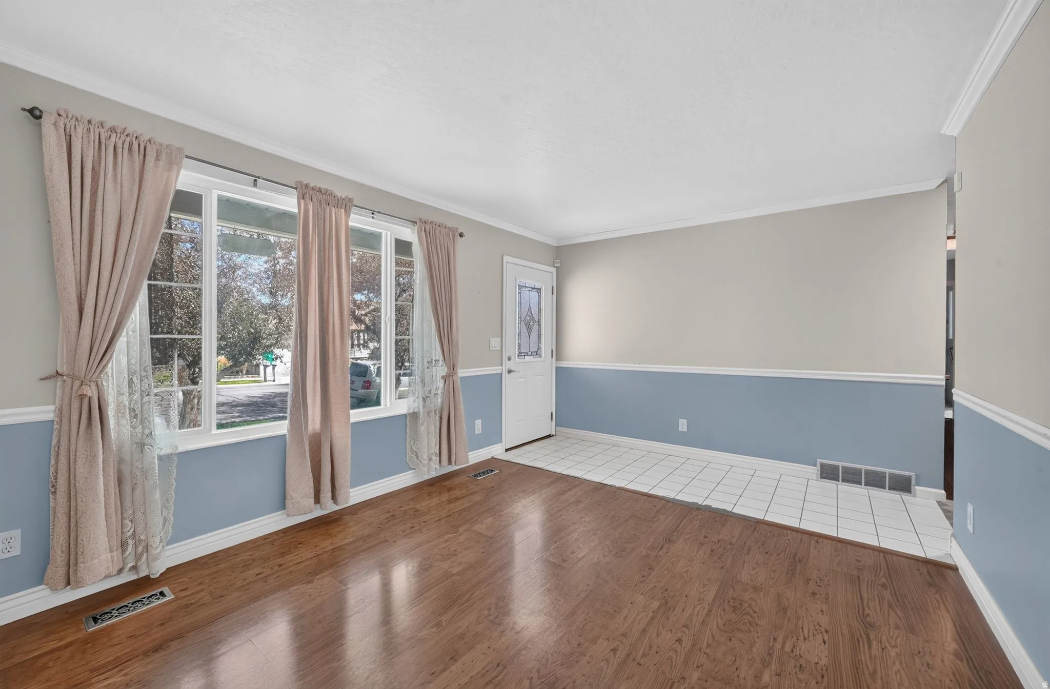 Hardwood-finish flooring, white trim, white wall paneling, white ceiling, and a paneled entry door with decorative glass