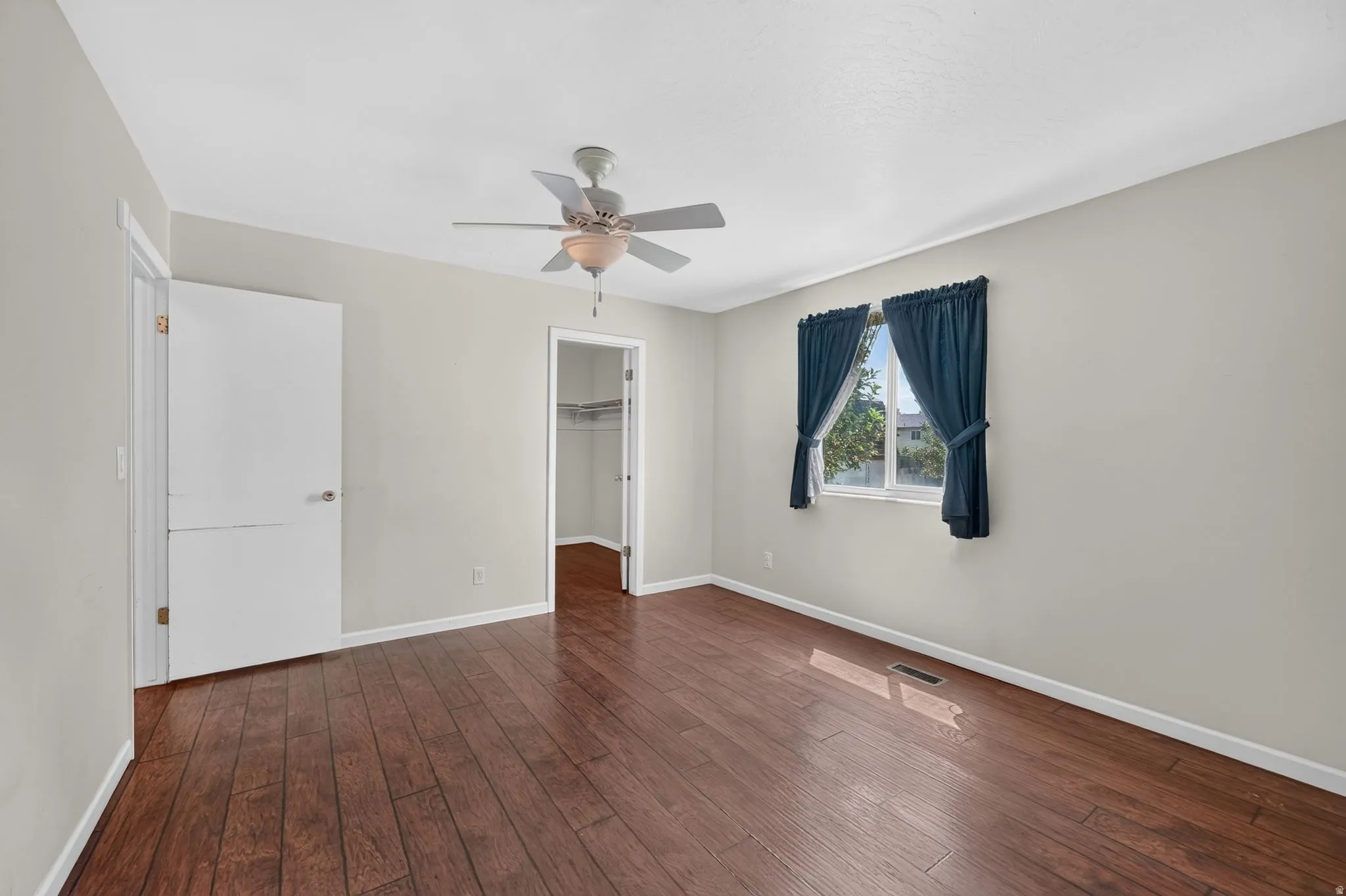 Wood-finish flooring with a ceiling fan, a window, and a closet with built-in shelving