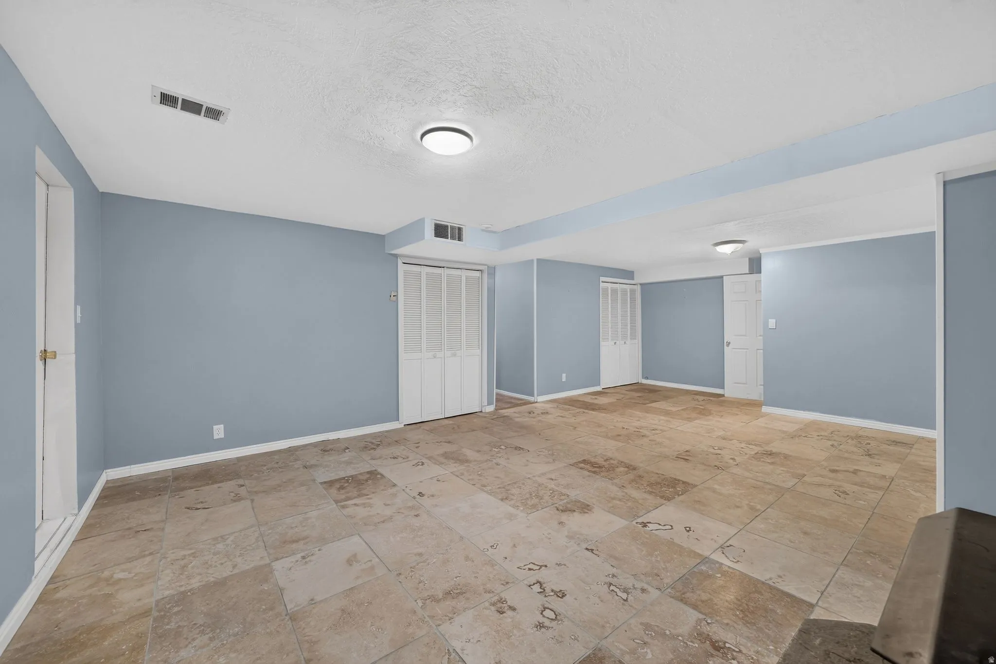 Expansive room featuring large format tile flooring, multiple doors, and overhead lighting