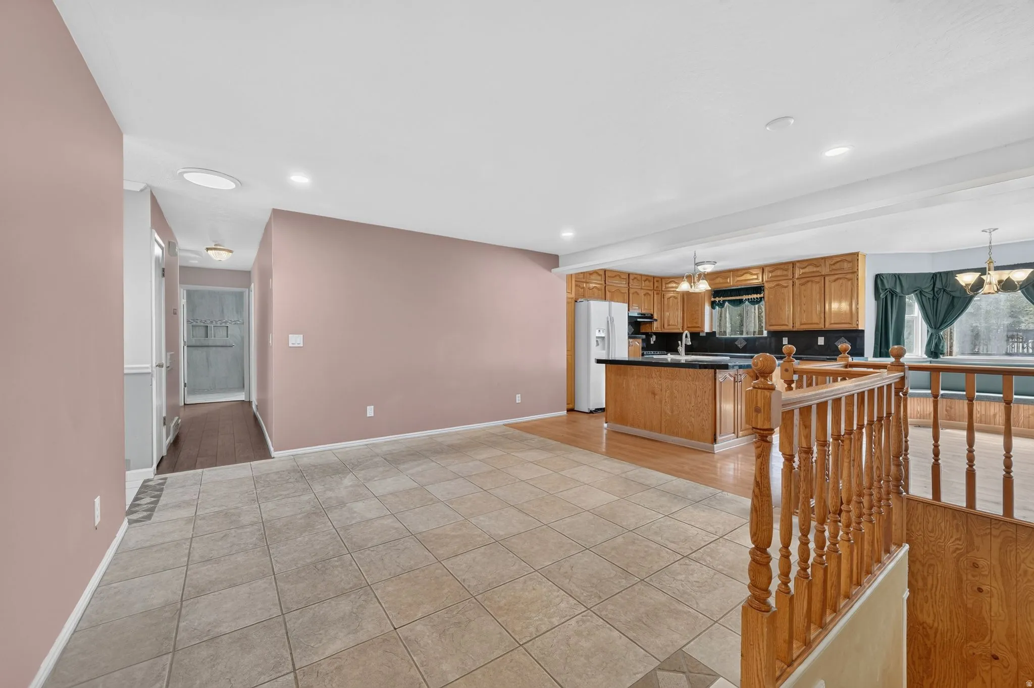 Tiled flooring entry area, wood-finish flooring in kitchen, kitchen with wood cabinetry, kitchen island with dark counter, and staircase with wood railing