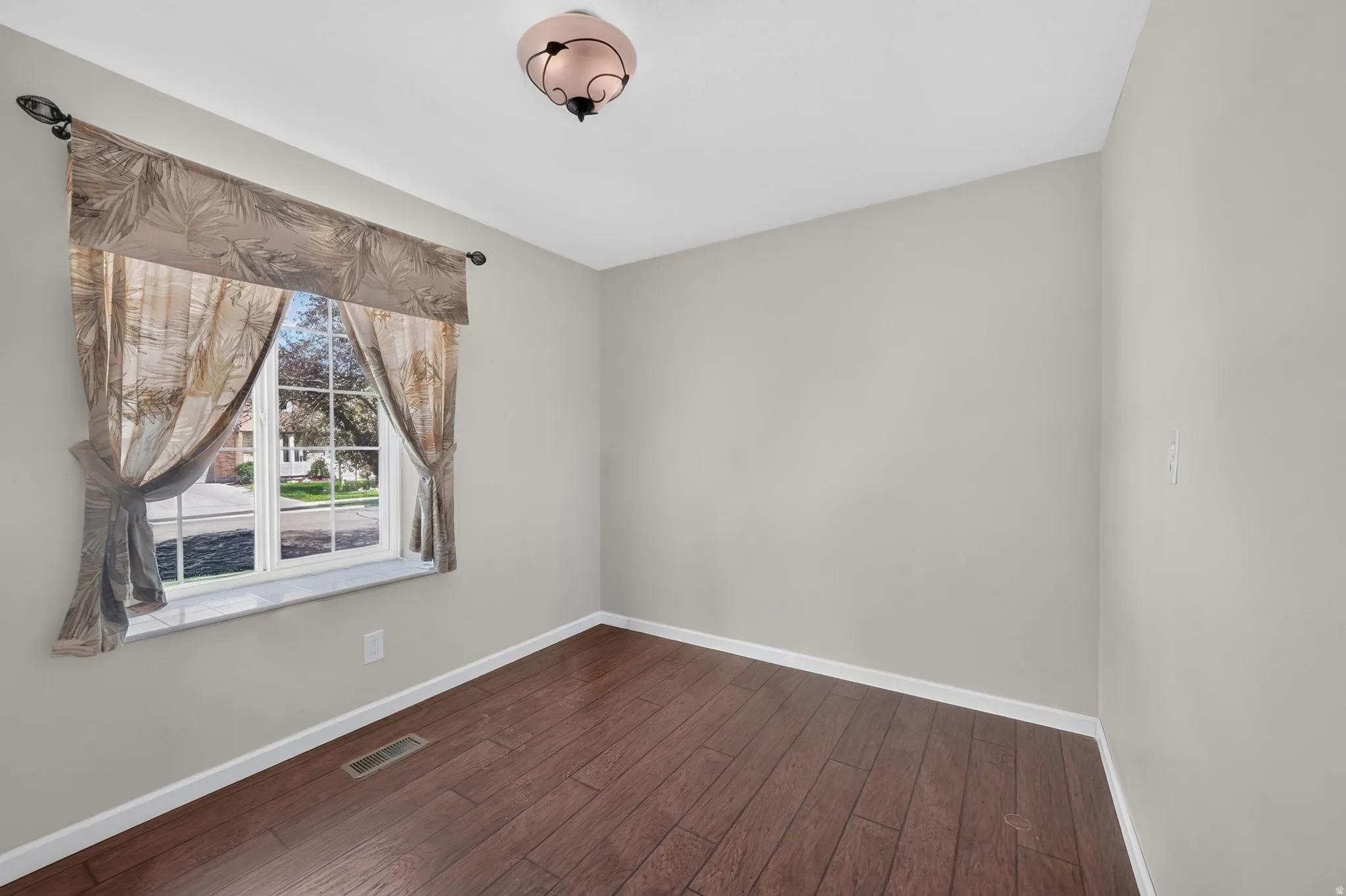 Wood-finish flooring, light gray wall color, a single window, and a ceiling-mounted light fixture
