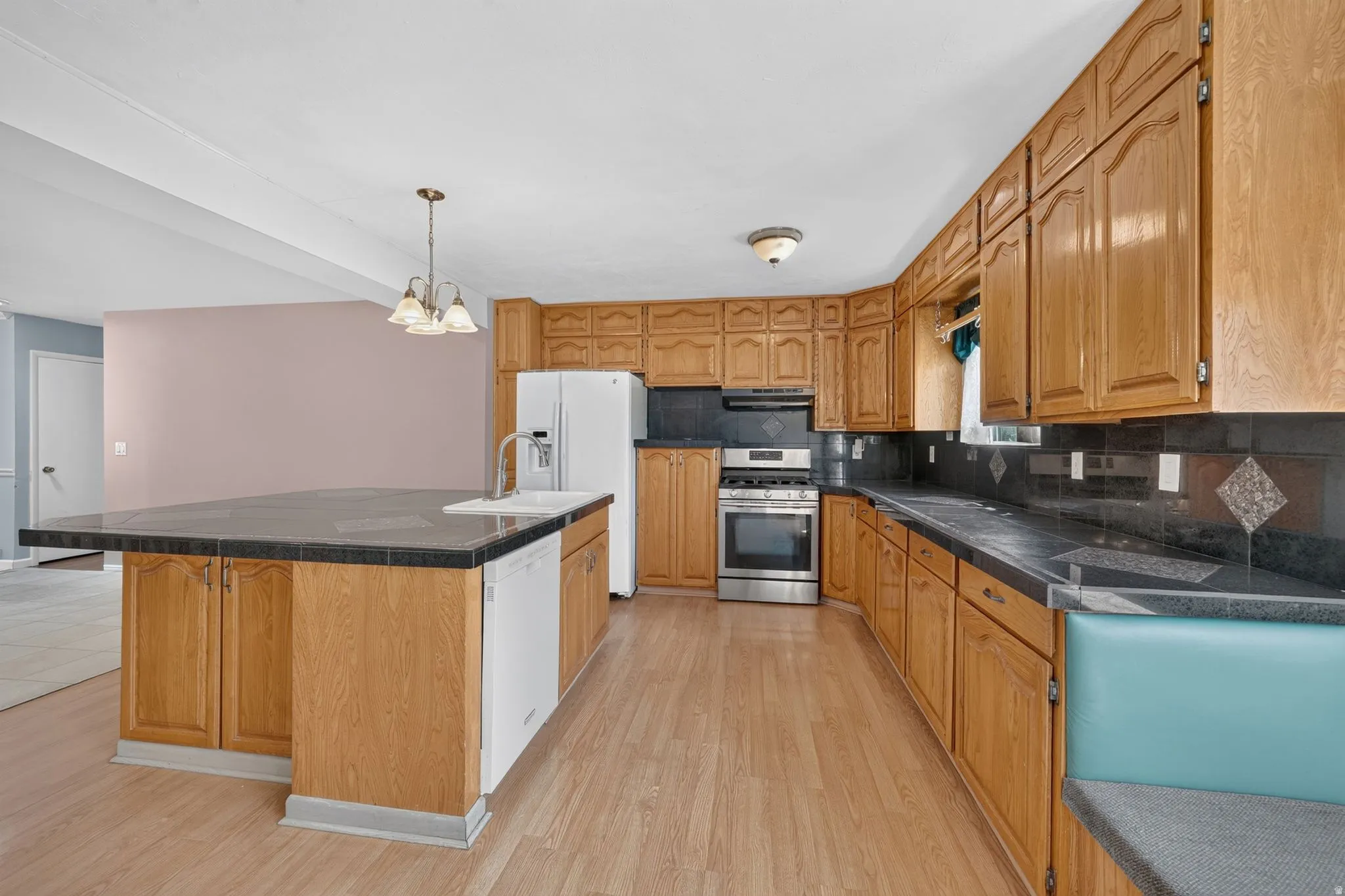 Kitchen featuring wood-finish flooring, wood cabinetry, a center island with a sink, stainless steel range, and tile countertops