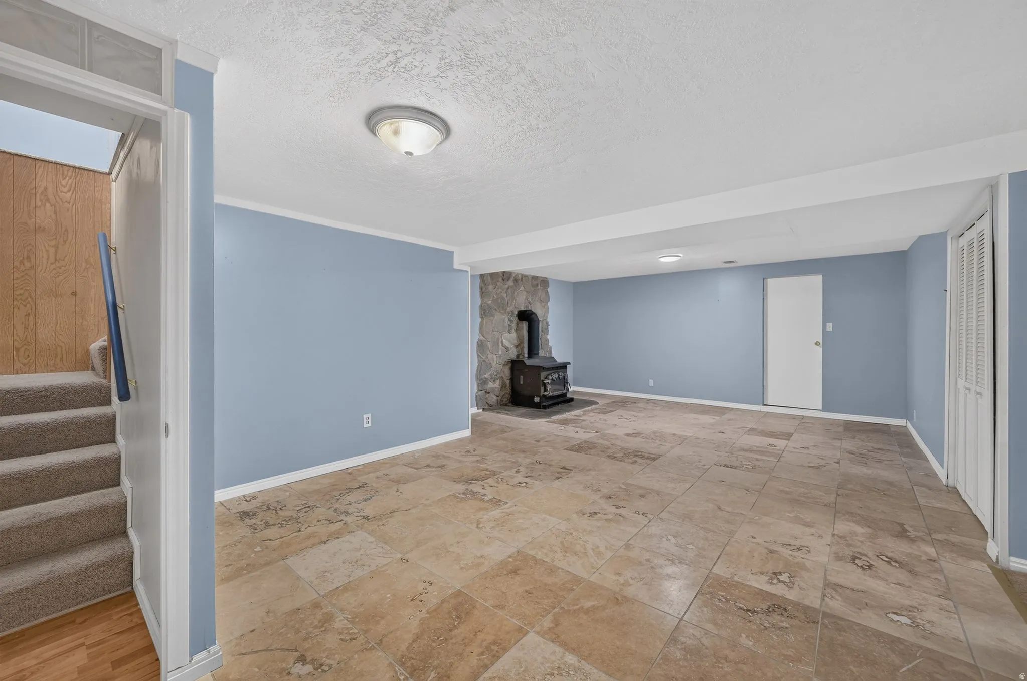 Spacious room featuring tile flooring, a stone-clad wall with a wood-burning stove, and a white bi-fold closet door