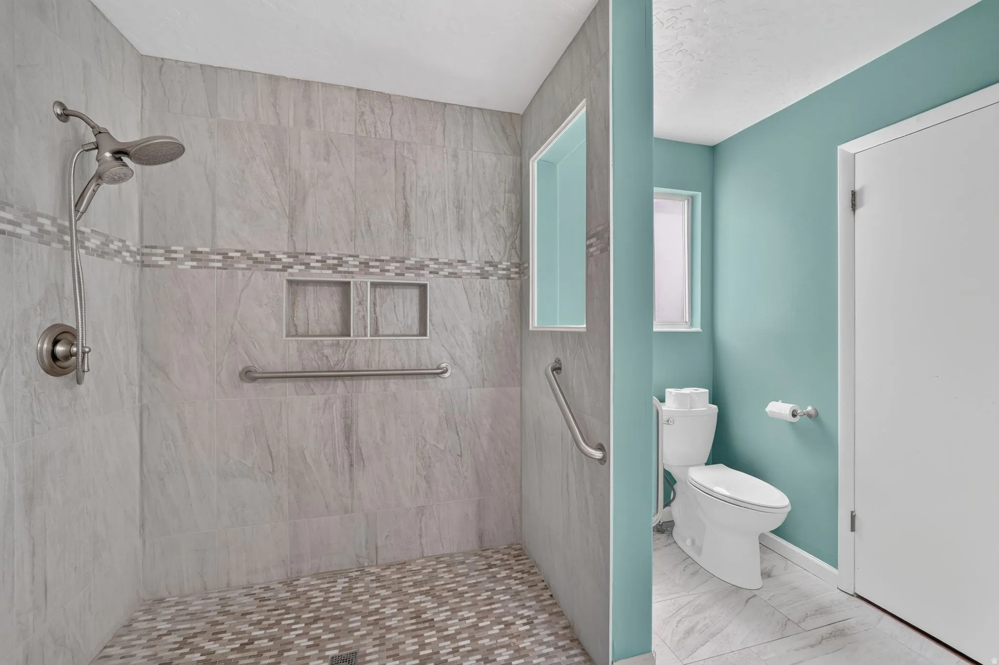 Walk-in shower with tiled walls and floor, two recessed niches, and a handheld shower fixture