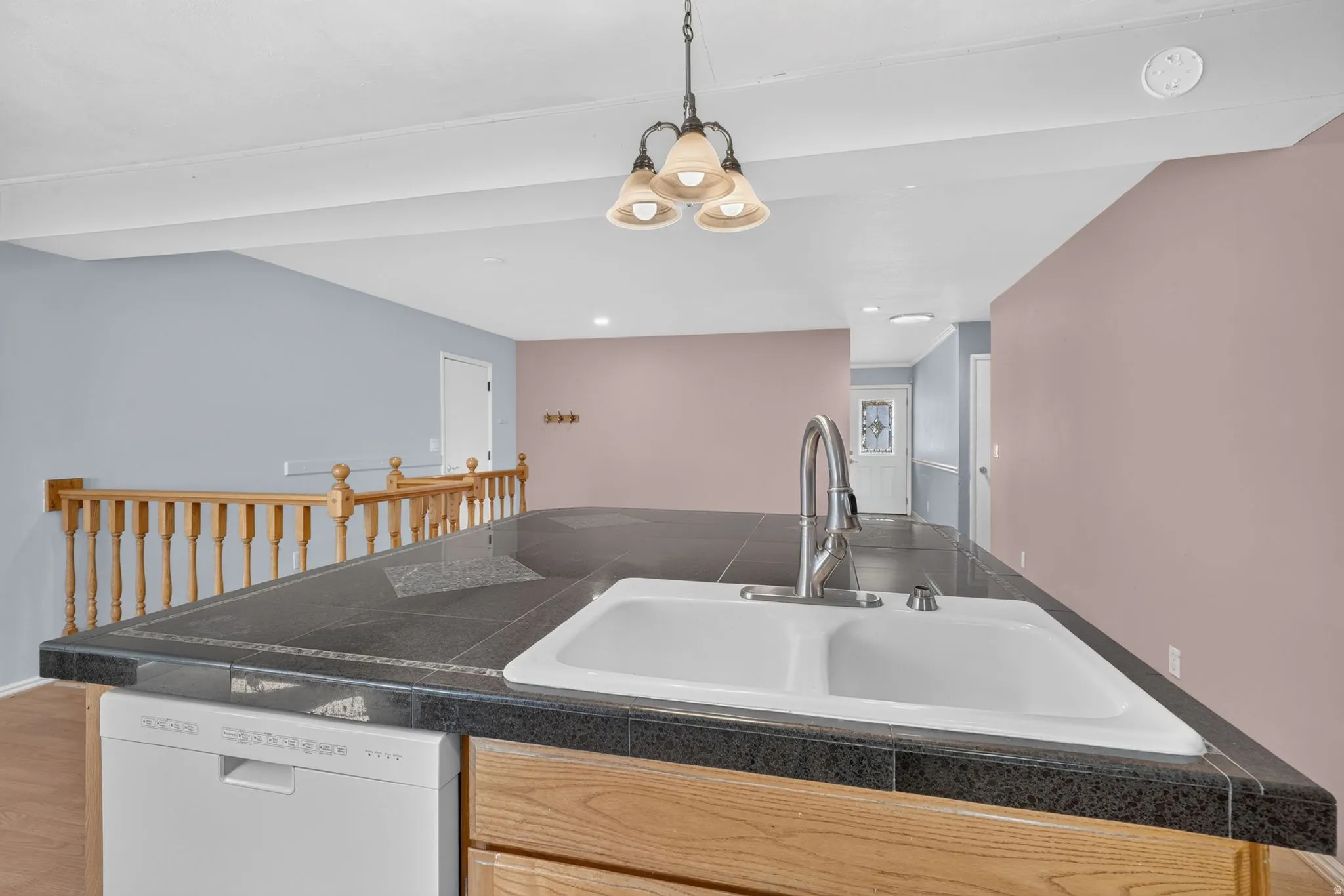 Kitchen island with tiled countertop, double basin sink with gooseneck faucet, built-in dishwasher, and wood-finish cabinetry