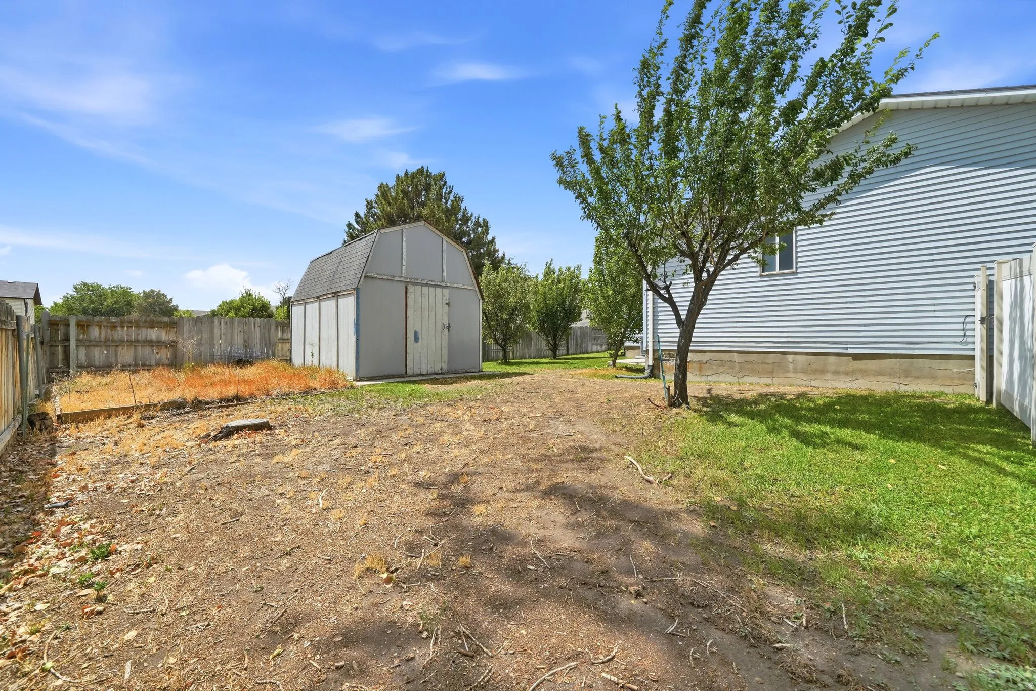 Spacious backyard featuring a storage shed, established tree, and a partial privacy fence