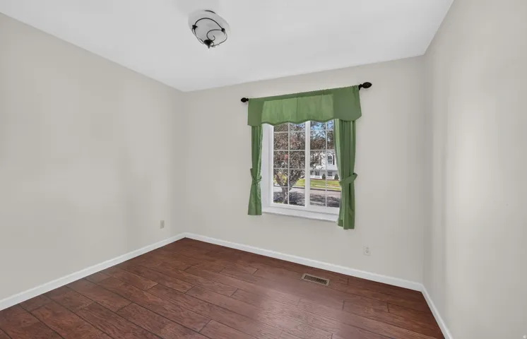 Bright corner bedroom with wood-finish flooring, large window with natural light, and fresh white walls