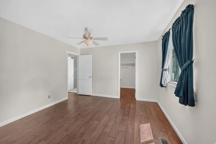 Wood-finish flooring with light-toned walls, featuring a ceiling fan with integrated lighting