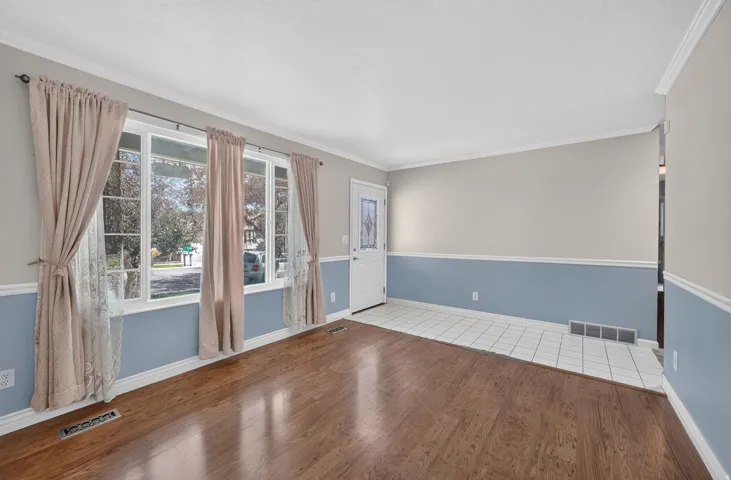 Hardwood-finish flooring, white trim, white wall paneling, white ceiling, and a paneled entry door with decorative glass