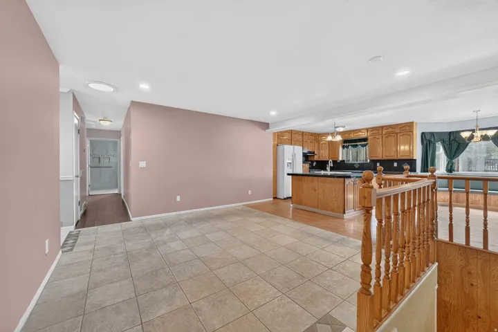 Tiled flooring entry area, wood-finish flooring in kitchen, kitchen with wood cabinetry, kitchen island with dark counter, and staircase with wood railing